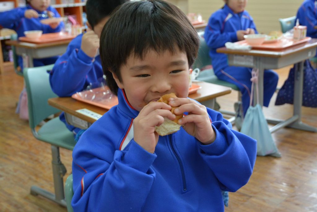 写真：赤身と脂のバランスがいい秋田由利牛と野菜を、パンにはさんだサンドイッチを食べる児童1
